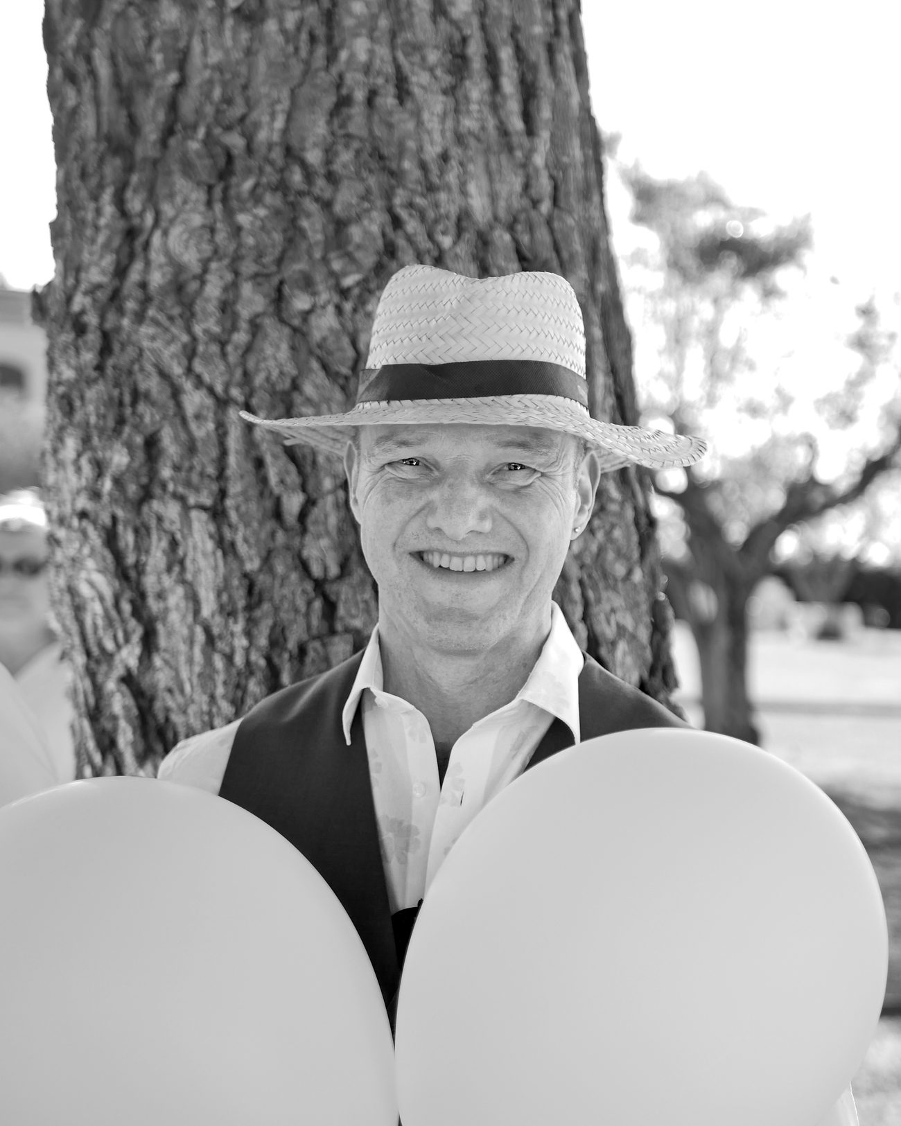Ritratto di un invitato con cappello di paglia e palloncini bianchi sotto un pino